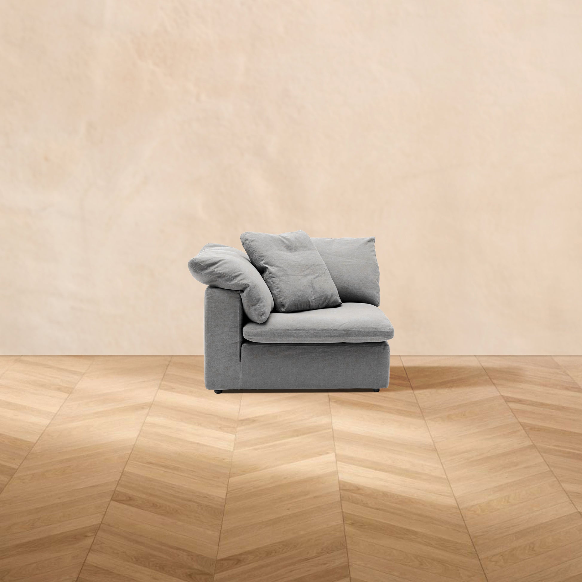 A HavenlyCloud® Couch Corner in Gray with performance fabric is centered on a wooden herringbone floor, set against a plain beige wall in the background.