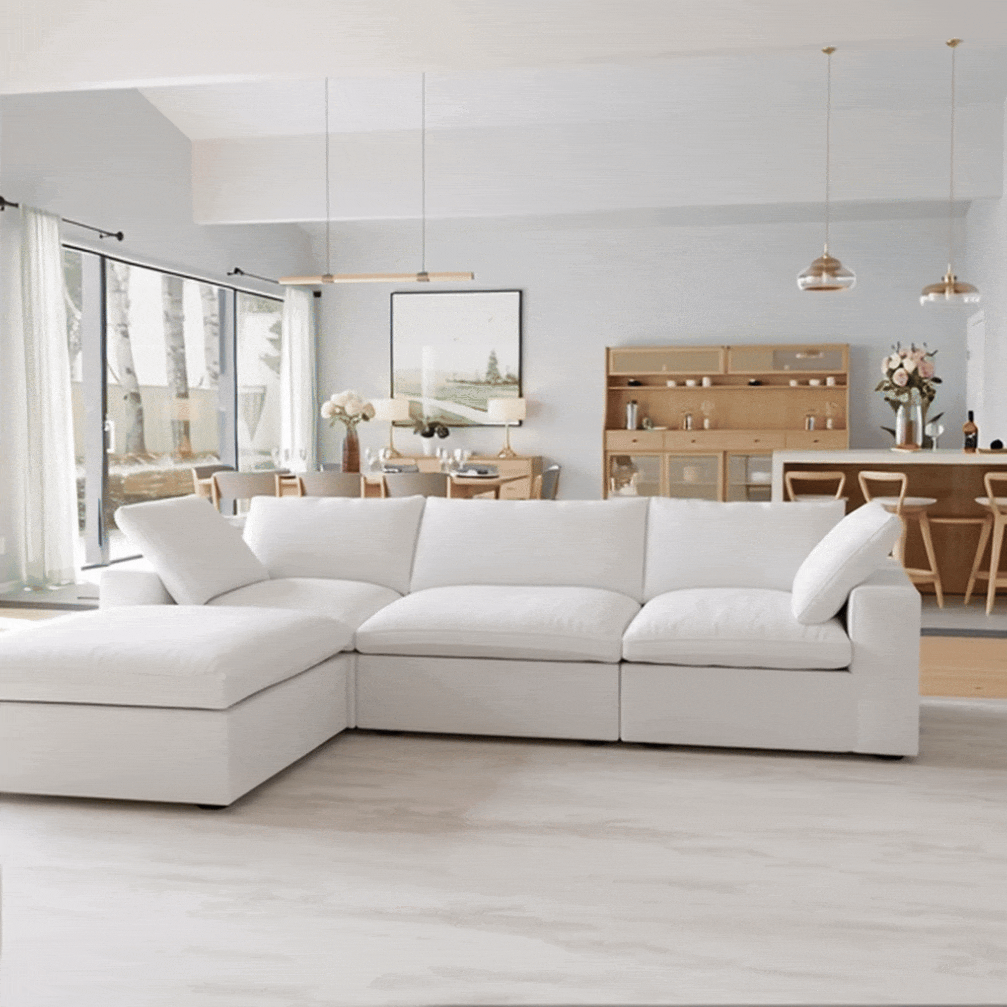 A modern living room with the CloudForm™ 3-Seater + Ottoman Modular Sofa in white, a light wood dining set, pendant lights, and large windows that fill the space with natural light.