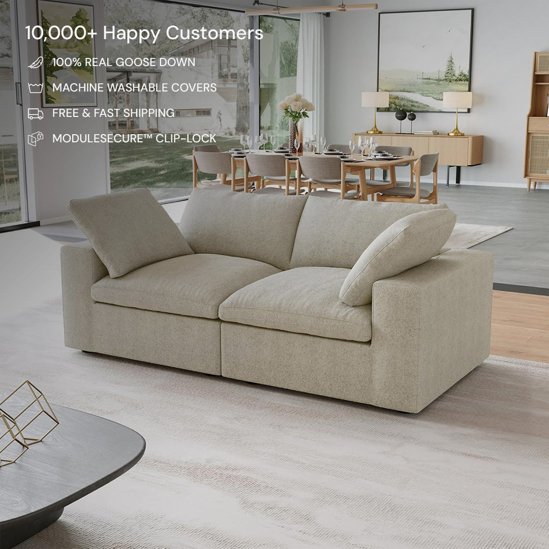 The CloudForm™ 2-Seater Modular Sofa in beige features plush cushions and removable fabric covers, complementing a modern living room with large windows, a dining area, and minimalist decor—earning high customer satisfaction.