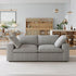 A modern living room showcases a Sofatica® Modular 2-Seater Cloud Couch in gray performance fabric, paired with a wooden dining table and chairs, cabinets, pendant lights, and decorative accents in the background.