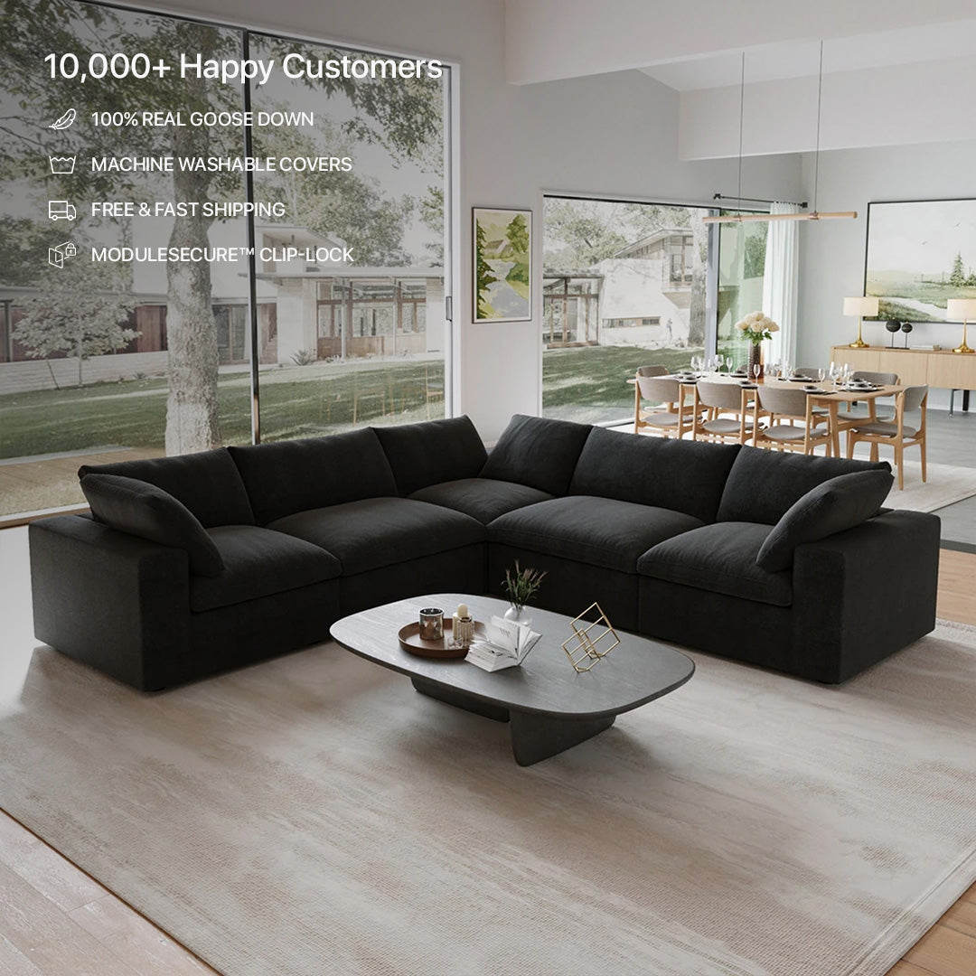 The CloudForm™ 5-Seater Modular L-Sofa in black, shown with a coffee table on a light rug in a modern living room with large windows; features removable fabric covers and emphasizes customer satisfaction.